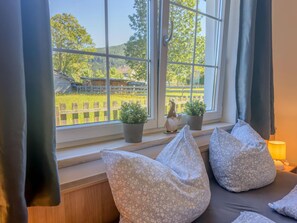 A room with a large window, a wooden bench with floral cushions, and two potted plants on the windowsill. - Spacious Alpine holiday apartment on the slopes (Sankt Margarethen im Lungau)