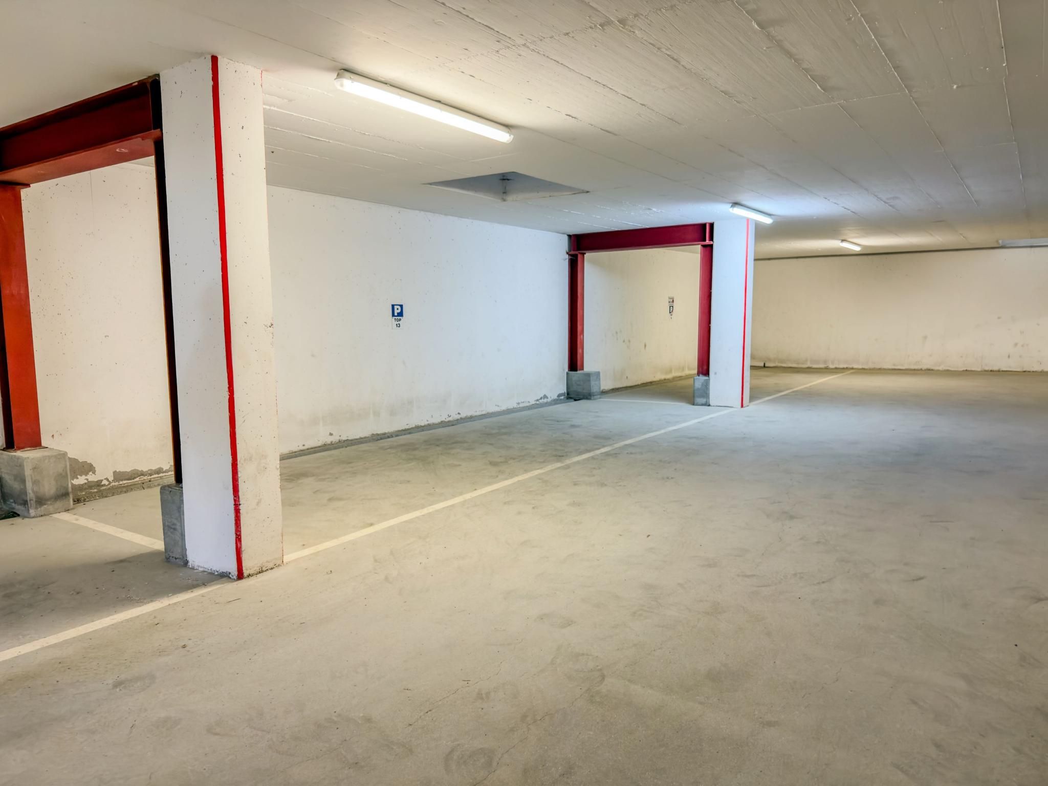 A parking garage with concrete floors and red-painted columns.
