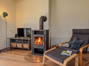Un salon chaleureux avec une cheminée moderne, un fauteuil confortable, un téléviseur à écran plat et une petite table avec des magazines.