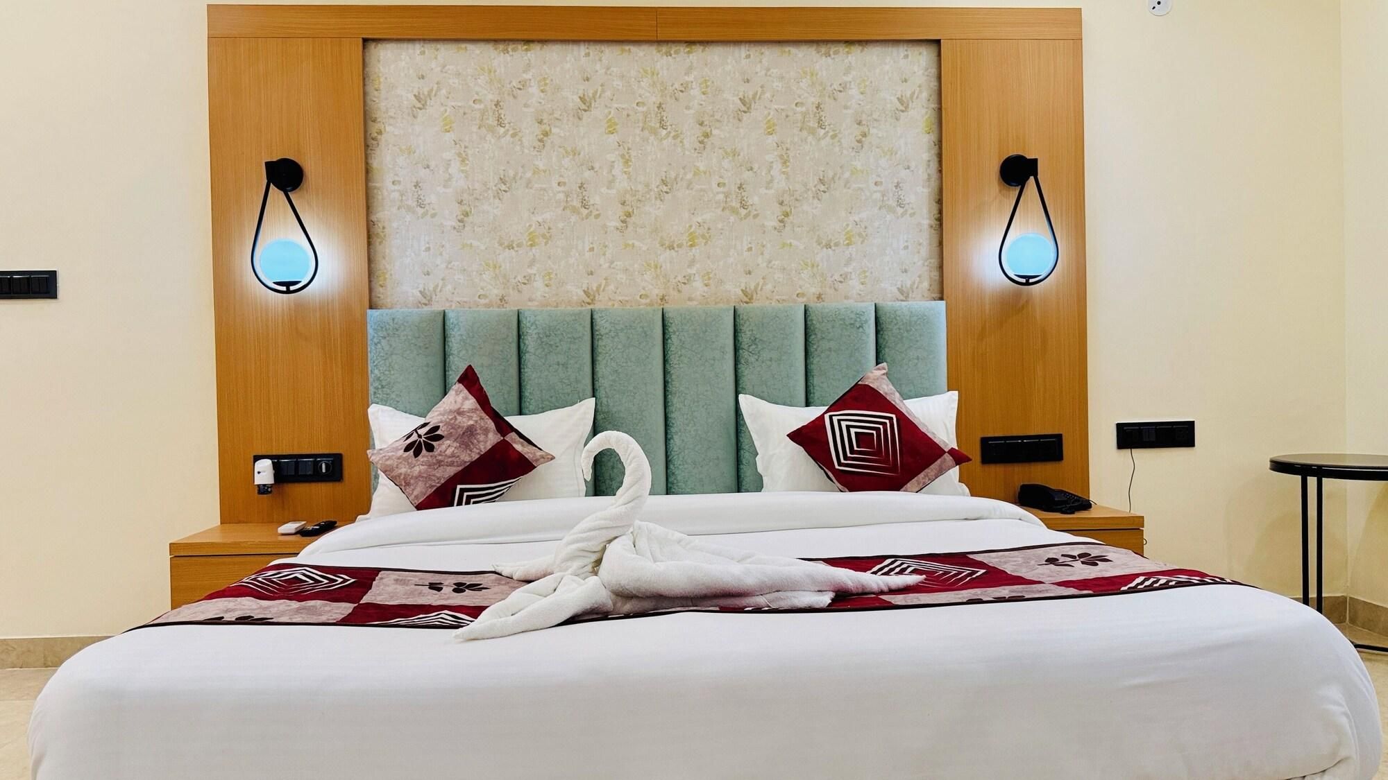 A hotel room with a bed, a headboard, two wall-mounted lights, a nightstand, and a bedside table.