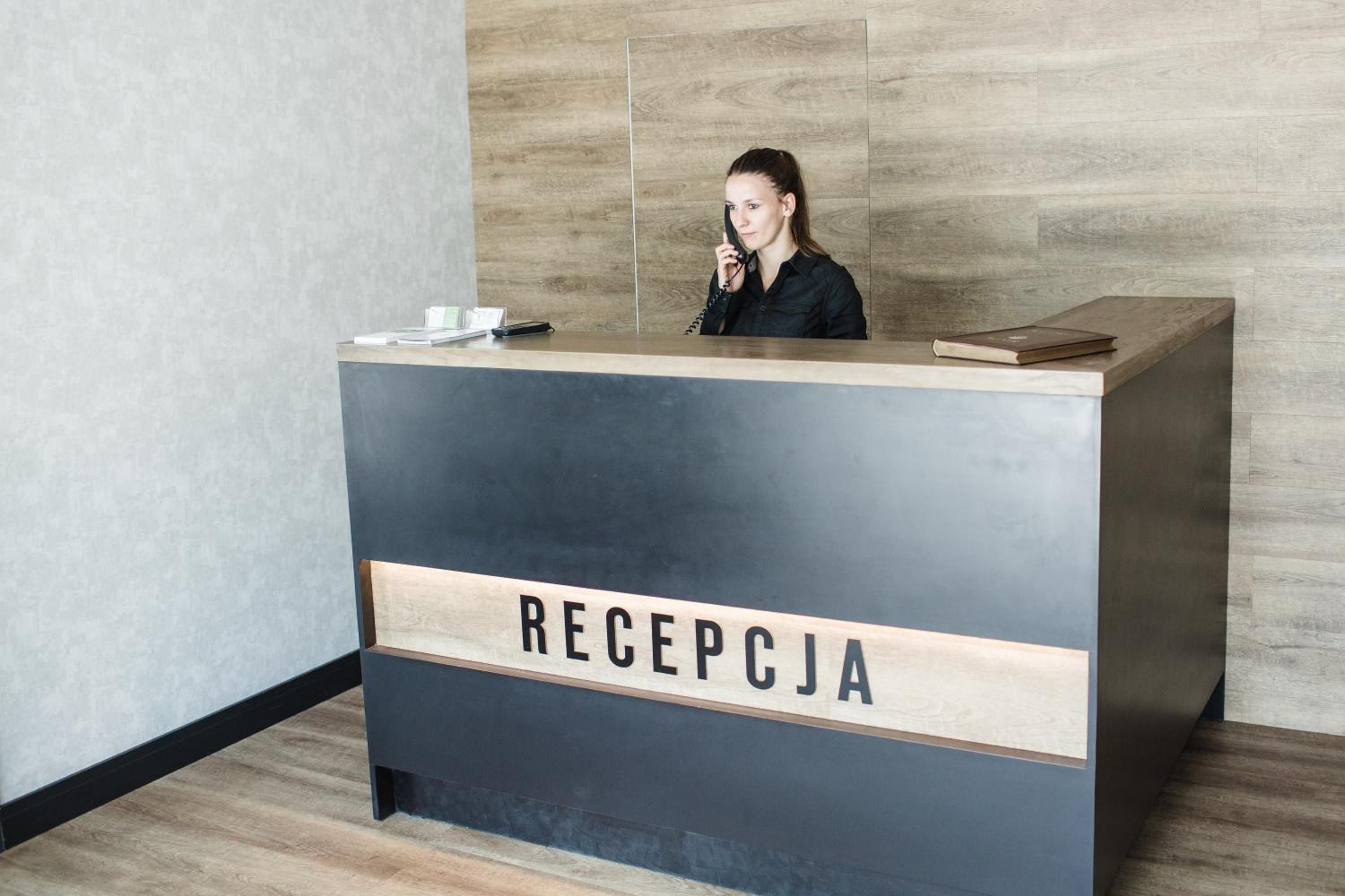 Ein Empfangsbereich mit einem Schild, auf dem 'RECEPCJA' steht, in einem modernen Innenraum mit Holzvertäfelung.