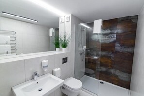Un baño moderno con cabina de ducha de vidrio, un lavamanos blanco y un inodoro.
