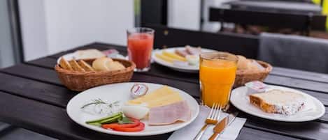 Una mesa servida con alimentos para el desayuno, incluyendo pan, huevos, queso, jamón y un vaso de jugo de naranja.