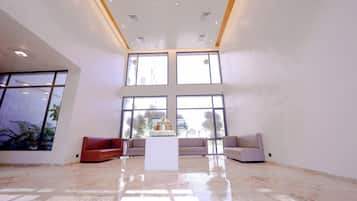 A spacious lobby with a high ceiling, large windows, and a polished marble floor.