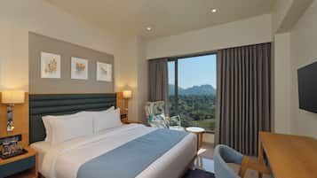 A hotel room with a large bed, a desk, a chair, and a view of the mountains.