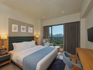 A hotel room with a large bed, a desk, a chair, and a view of the mountains.