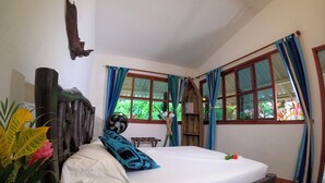 Una habitación con una cama, cabecera de madera, ventana con cortinas y un ventilador.