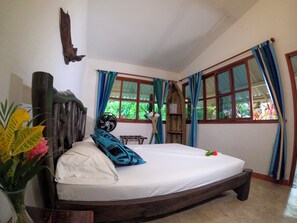 Una habitación con una cama, cabecera de madera, ventana con cortinas y un ventilador.