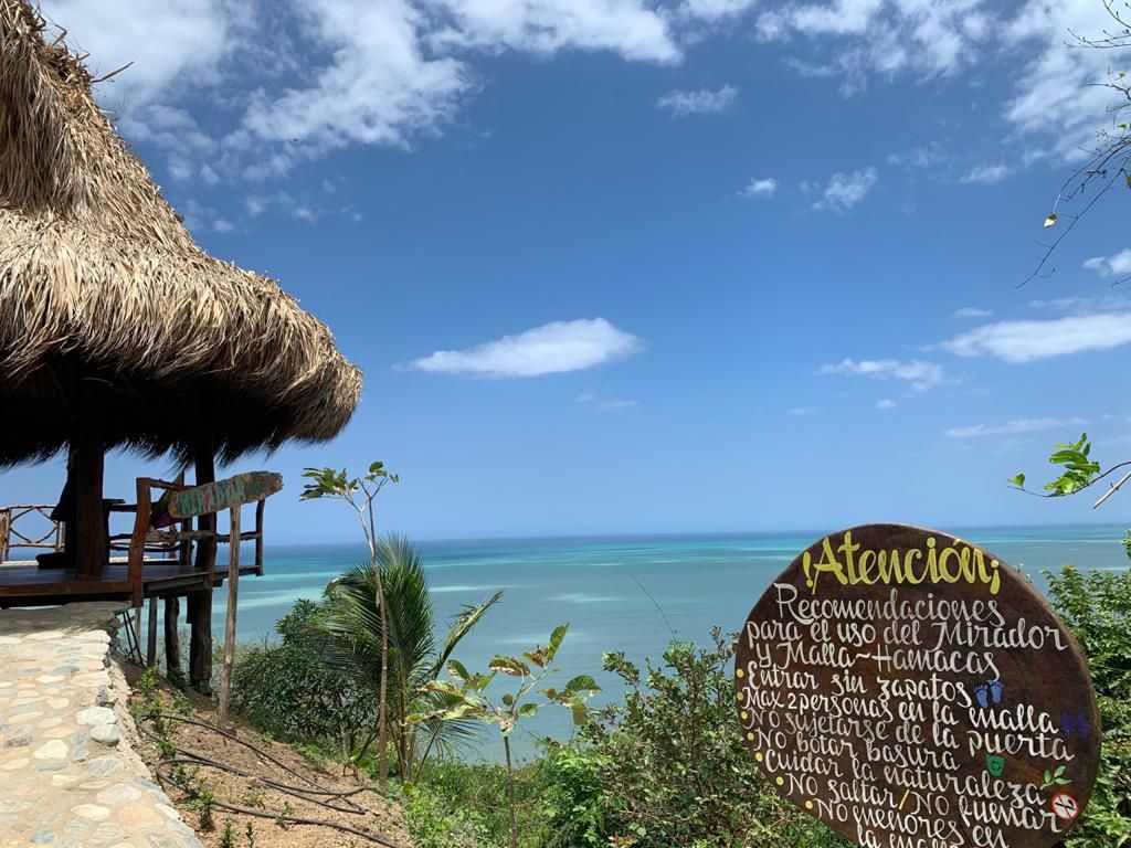 Vista de la playa con una estructura de techo de paja y un letrero de madera con texto.