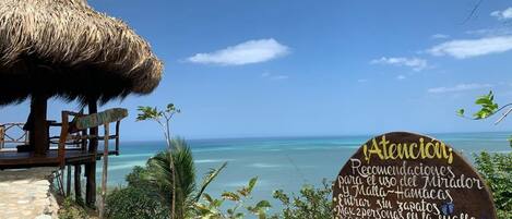 Vista de la playa con una estructura de techo de paja y un letrero de madera con texto.