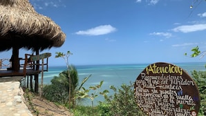 Vista de la playa con una estructura de techo de paja y un letrero de madera con texto.