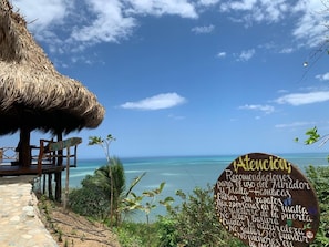Vista de la playa con una estructura de techo de paja y un letrero de madera con texto.