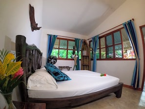 Una habitación con una cama, cabecera de madera, ventana con cortinas y un ventilador.