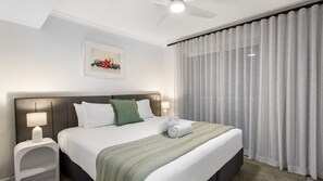 A hotel room with a bed, a bedside table, a lamp, a ceiling fan, and a window with curtains. - Golden Beach Sundown | Waterfront & Sunset Views (Golden Beach)