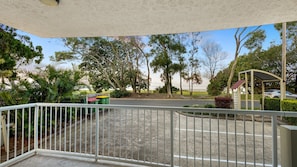 A balcony with a view of a parking area, trees, and a building with a red roof. - Golden Beach Sundown | Waterfront & Sunset Views (Golden Beach)