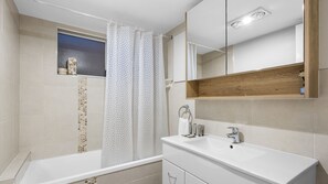 Ein modernes Badezimmer mit Badewanne, Duschvorhang, Waschtisch und Spiegel sowie einem kleinen Fenster.