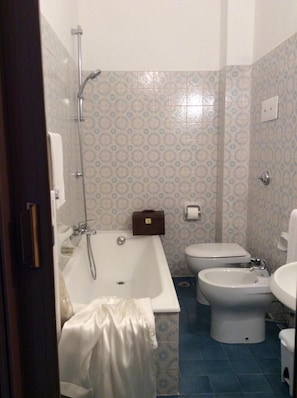 Une salle de bain avec une baignoire, deux toilettes, un bidet et une douche.