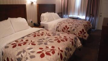 A hotel room with two beds, each with a floral bedspread, a wooden headboard, a bedside table with a lamp, and a window with curtains.