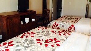 Ein Hotelzimmer mit zwei Betten, einem Fernseher auf einer Holzkommode, einem Sessel und einer Tür zu einem anderen Raum.
