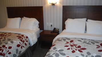 A hotel room with two beds, a nightstand with a phone, and a wall-mounted light.