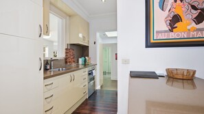 A kitchen with a sink, cabinets, and a countertop. There is a door leading to another room. - The Brick House East Melbourne (East Melbourne)