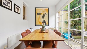 A dining area with a long wooden table, brown leather chairs, a framed poster on the wall, and a view of the outdoors through large windows. - The Brick House East Melbourne (East Melbourne)