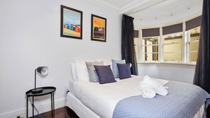 Une chambre d’hôtel avec un lit, des oreillers, une table de chevet, une lampe et deux tableaux encadrés accrochés au mur.