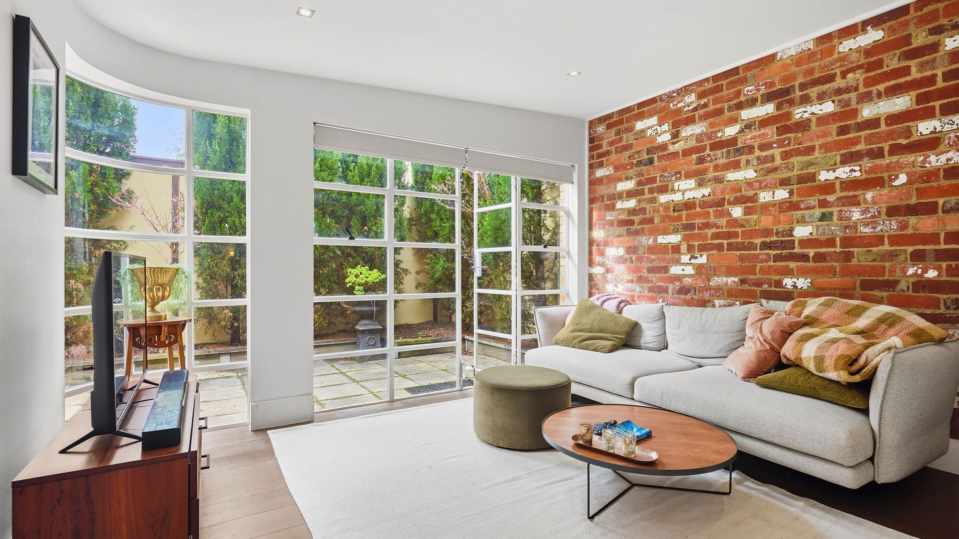 A modern living room with a white sofa, a coffee table, and a brick wall.