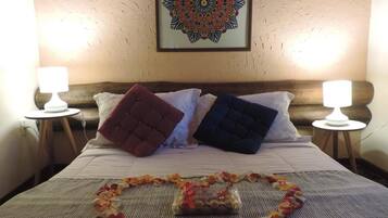 Cama bem arrumada com uma guirlanda decorativa em formato de coração de flores, uma obra de arte com mandala emoldurada acima da cama e duas luminárias laterais em mesas de cabeceira de madeira.