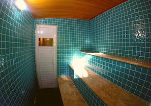 Un baño con paredes de azulejos azules, una puerta blanca y un banco.