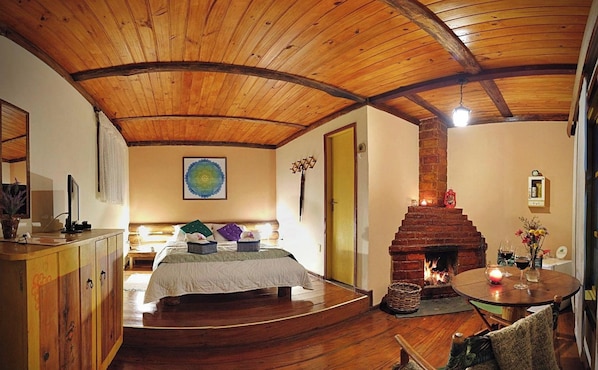 Una habitación con techo de madera, una cama con cubrecama blanco, chimenea y una mesa redonda con velas.