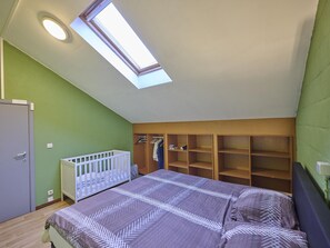 A bedroom with a skylight, a crib, a bed, and built-in shelving.