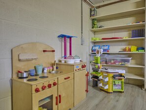A play kitchen with a sink, stove, and shelves with toys and storage bins.