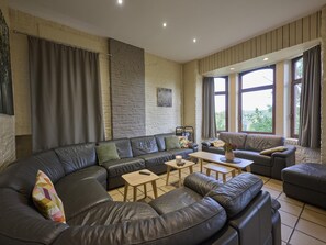 A modern living room with a large L-shaped black leather sofa, a wooden coffee table, and a stone accent wall.