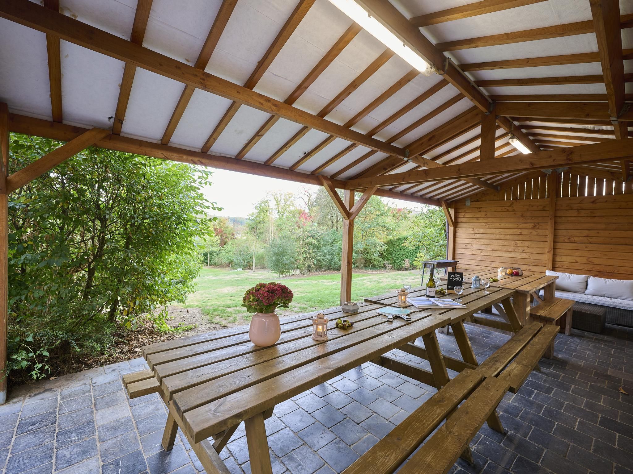 A covered outdoor area with a wooden table and benches, a garden view, and a sign reading 'villa to you'.