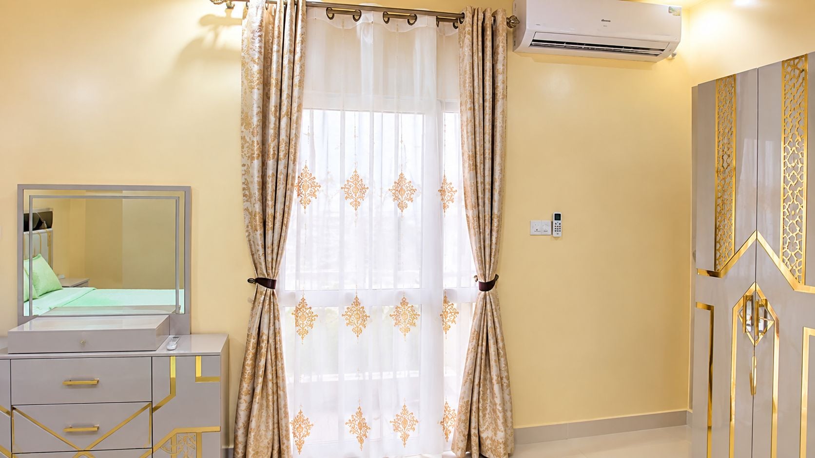Una habitación con una cama, una mesita de noche con espejo, un armario y una ventana con cortinas.