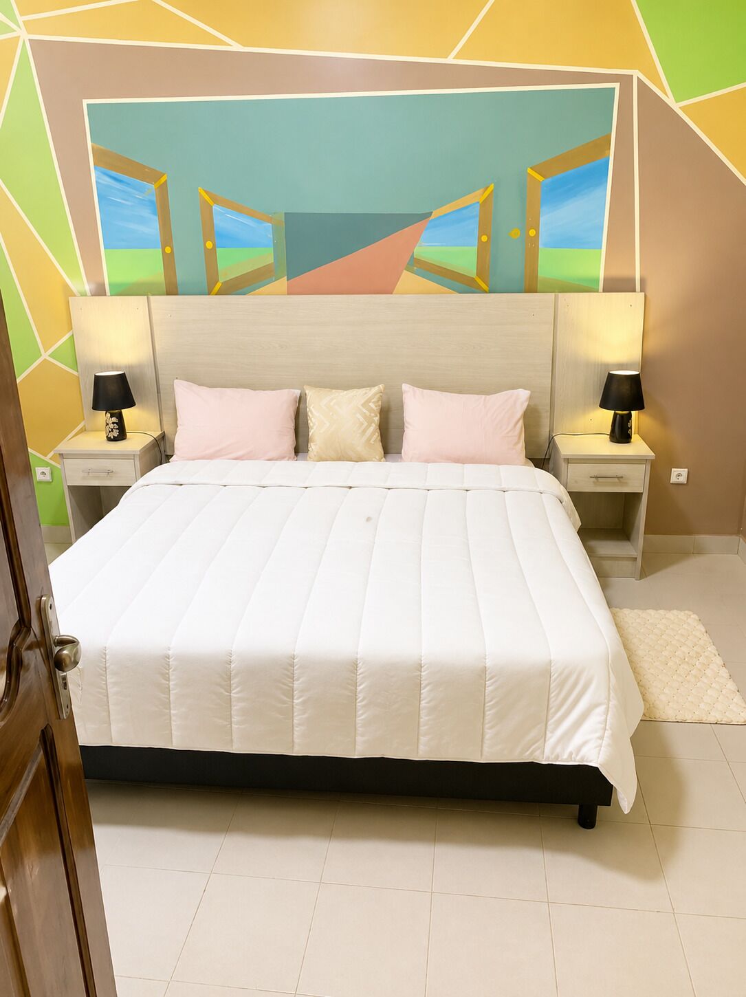 A bed with a white quilt, two bedside tables with lamps, and a wall with a geometric pattern.