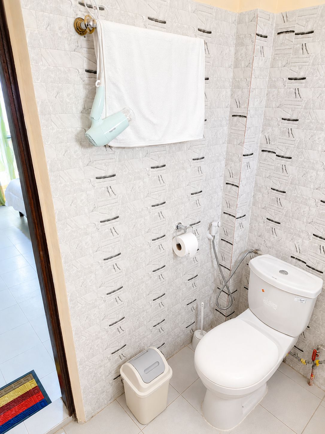 Un baño con inodoro, toallero, cabezal de ducha y dispensador de papel higiénico.