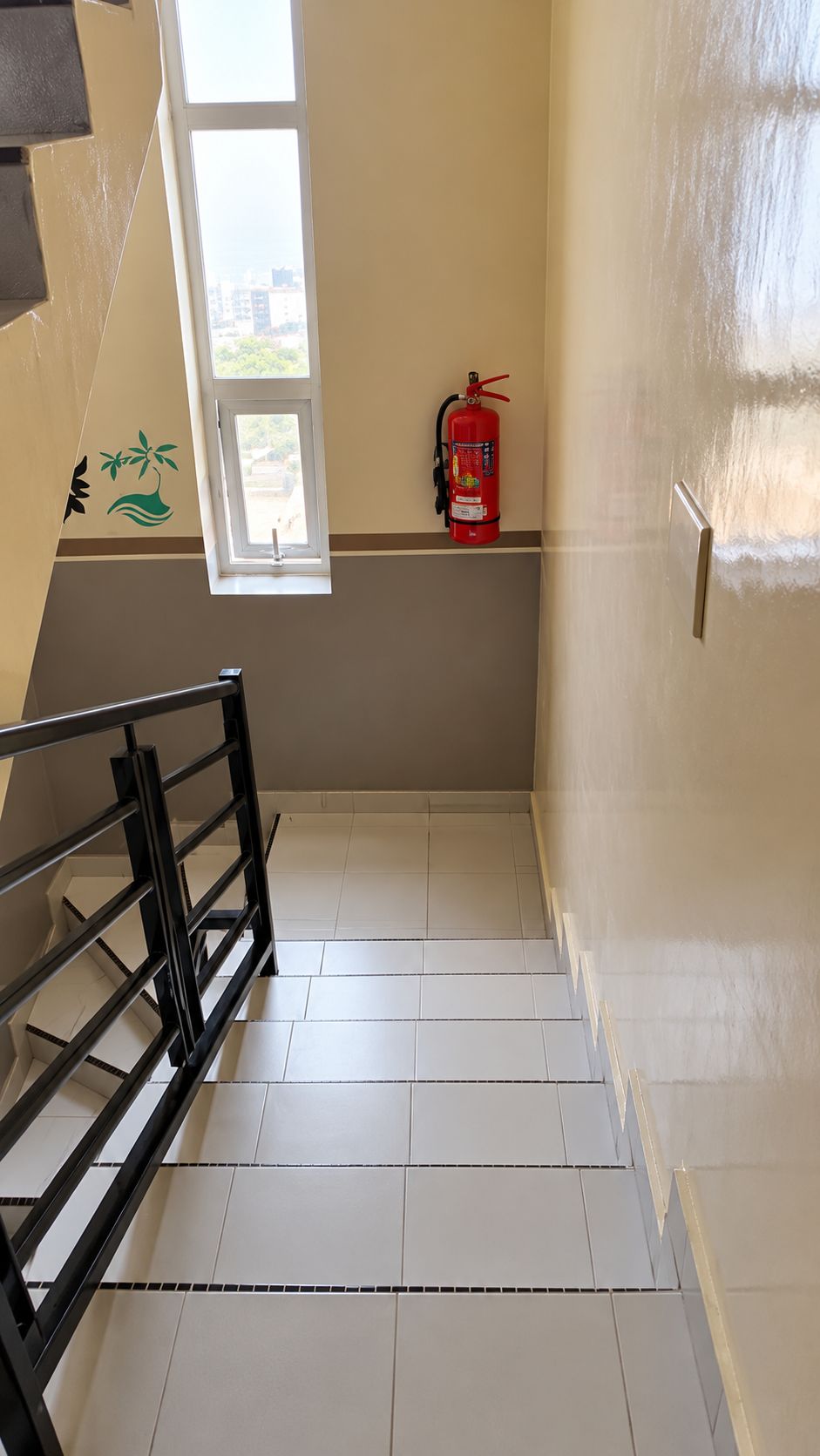 Una escalera con un extintor en la pared, un ventanal y una barandilla metálica.