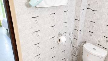 A bathroom with a toilet, a towel rack, a shower head, and a toilet paper holder.