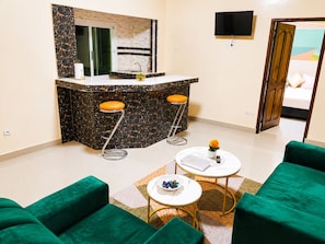 Un espacio habitable compacto con kitchenette, un televisor montado en la pared y un sofá verde.
