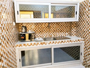 Una kitchenette con microondas, hervidor y pileta, frente a un muro con revestimiento de cerámica decorada.