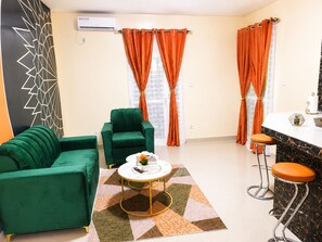 Una sala de estar con un sofá verde, una mesa redonda de centro y una zona de bar con taburetes.