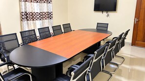 Un salón de conferencias con una mesa larga y sillas, un televisor en la pared y una puerta.