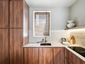 Eine moderne Küche mit Holzschränken, einer Edelstahl-Spüle und einem Fenster mit Jalousien.