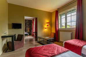 Una habitación de hotel con cama, escritorio, silla, televisión y ventana con cortinas.