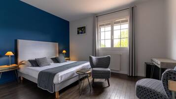 A bedroom with a large bed, two bedside lamps, a chair, a small table, and a window with curtains.