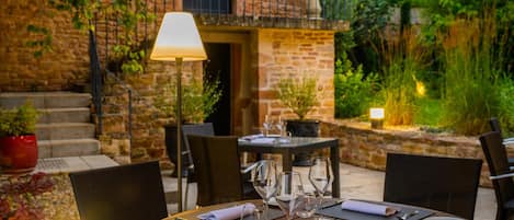 An outdoor dining area with a stone wall, a lamp, and a table set for two.