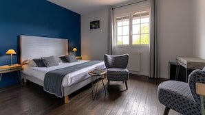 Ein Schlafzimmer mit einem großen Bett, zwei Nachttischlampen, einem Sessel, einem kleinen Tisch und einem Fenster mit Vorhängen.