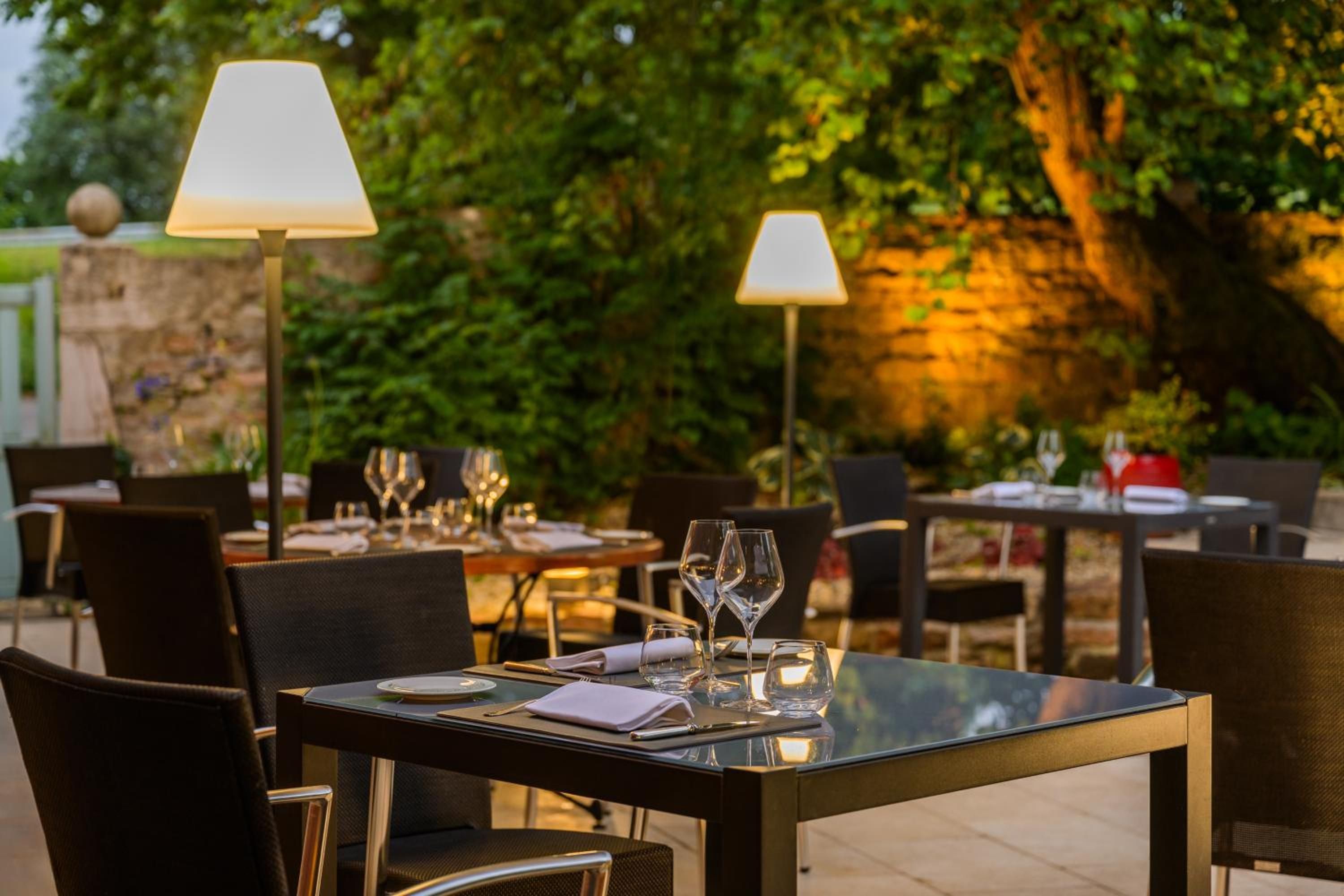 An outdoor dining area with tables set for two, each with a lamp and wine glasses.